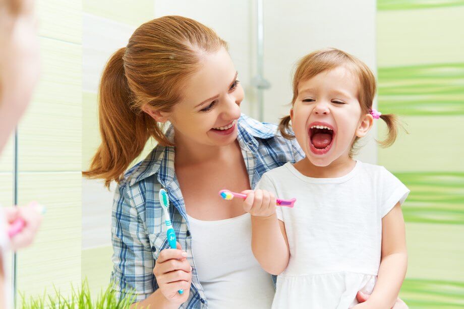 mother holding young daughter in front of mirror, holding toothbrushes